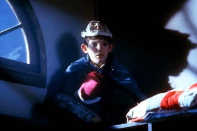 young boy curled up near an arched window at night with a har and wearing red gloves