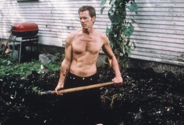 shirtless man in jeans digging a hole in his backyard