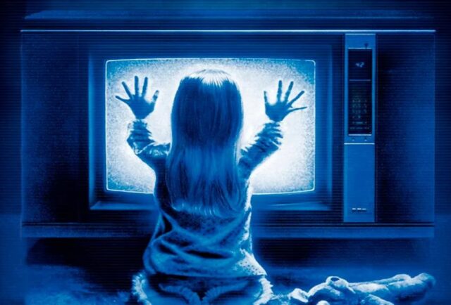 back view of little girl silhouetted against the TV glow; screen is all static and girl is holding both hands to the screen
