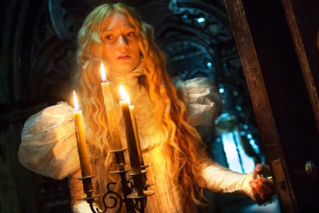 woman with long blonde hair in Gothic period dress holing a candelabra in a dark corridor