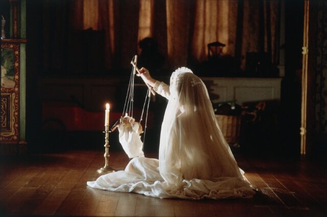 young girl, back to camera, dressed n white with a veil playing with a marionette