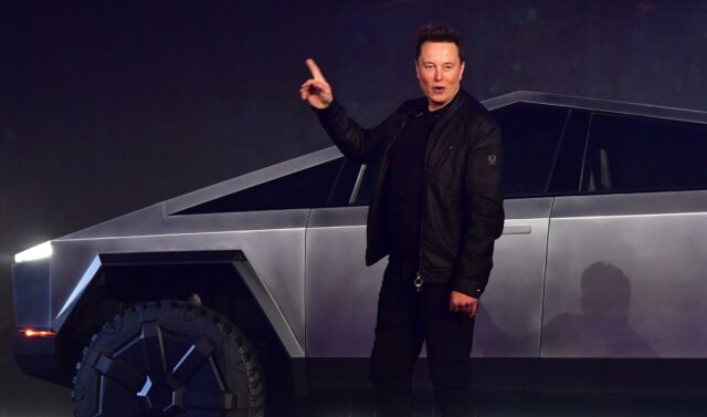 Tesla CEO Elon Musk speaks at an event while standing in front of a Cybertruck.