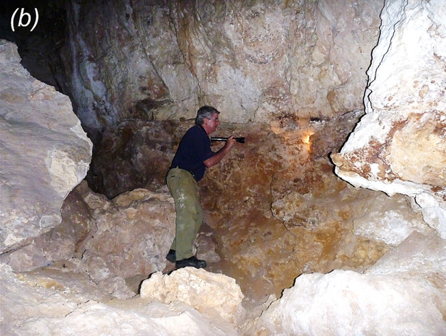 An man in khakis and a dark blue shirt studies a cave wall.