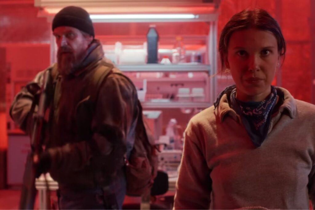 armed bearded middle aged man stands guard while a young woman focuses intently.