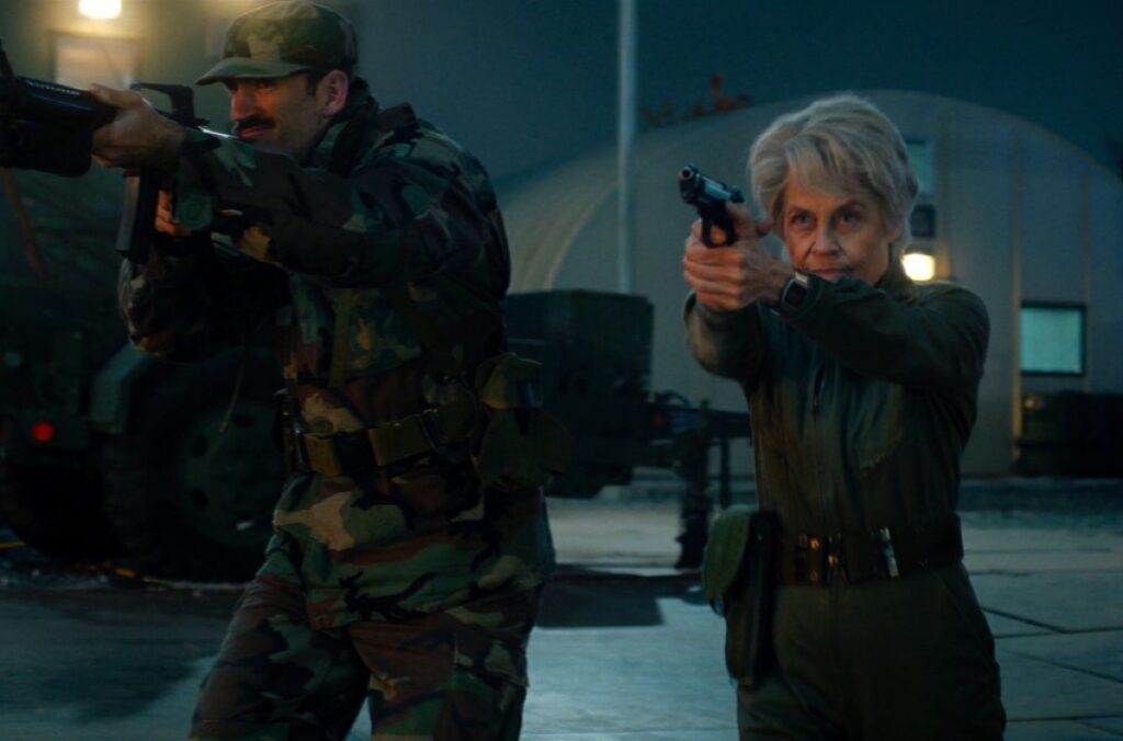 soldier and gray haired tough older woman aiming guns at an unseen antagonist.