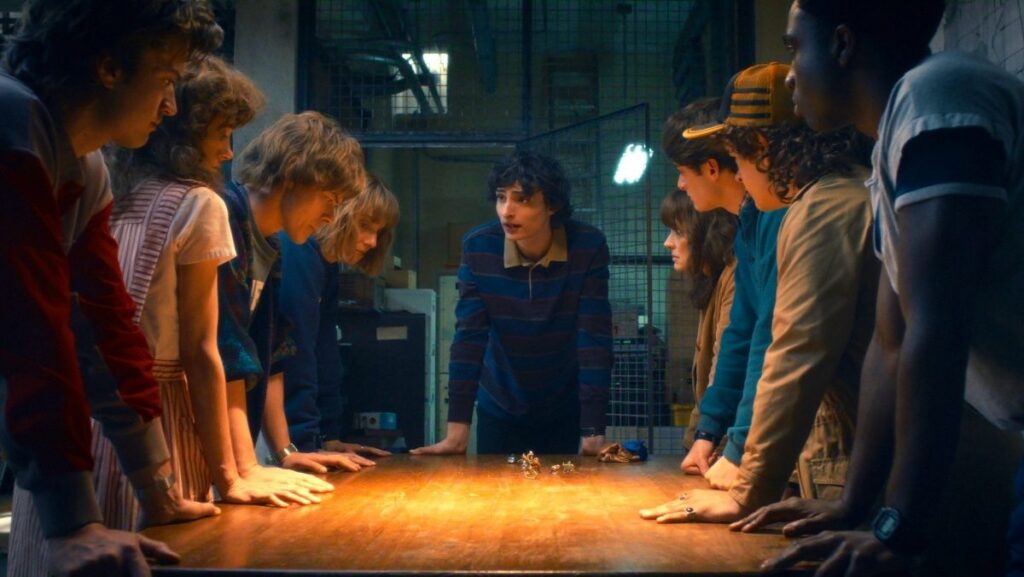 Group of young people standing around a table with a D&D board and pieces on it.