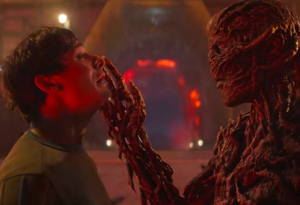 terrified young man faces vecna as the monster touches one icky hand to his face