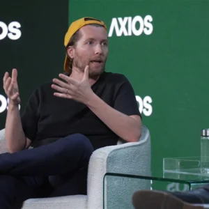 A man in a baseball hat talks and gesticulates on stage