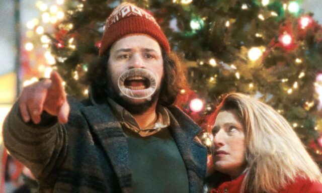 Un hombre con un sombrero tonto frente al árbol de Navidad atraca ante la cámara mientras una mujer mira y pone los ojos en blanco