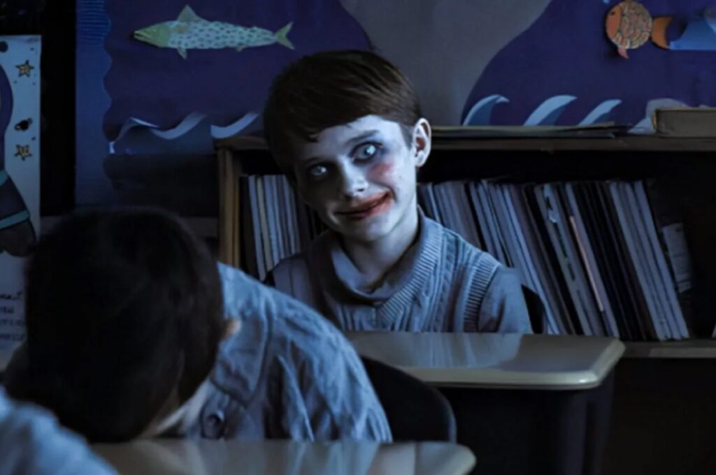 young boy in classroom with creepy clown makeup and a sinister smile
