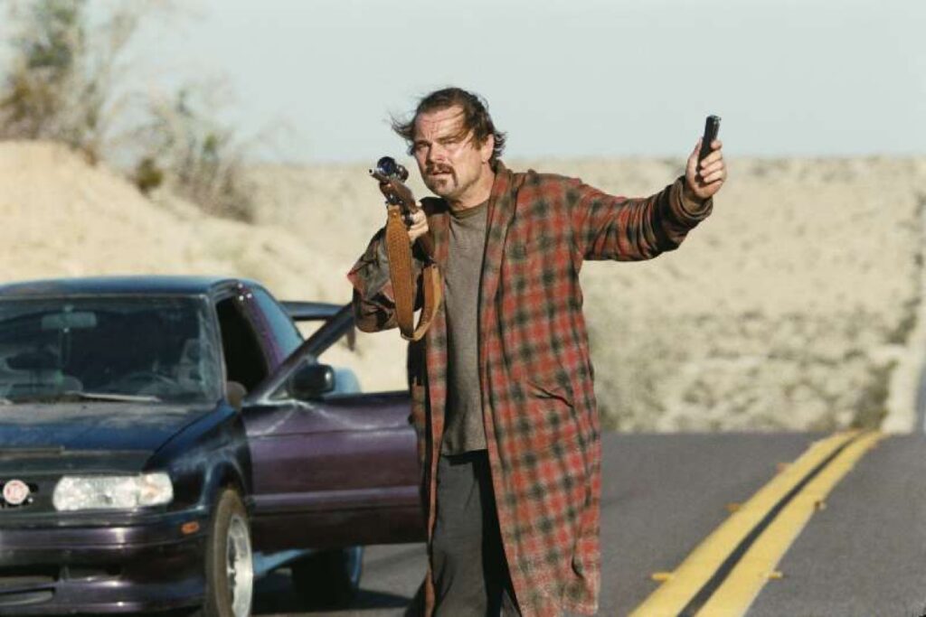 scruffy middle aged man long plaid shirt on a roadway, standing next to car with open door, pointing a gun with a camera phone in his other hand