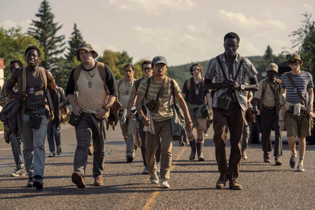 group of young boys walking as a group down a road with armed soldiers at the ready