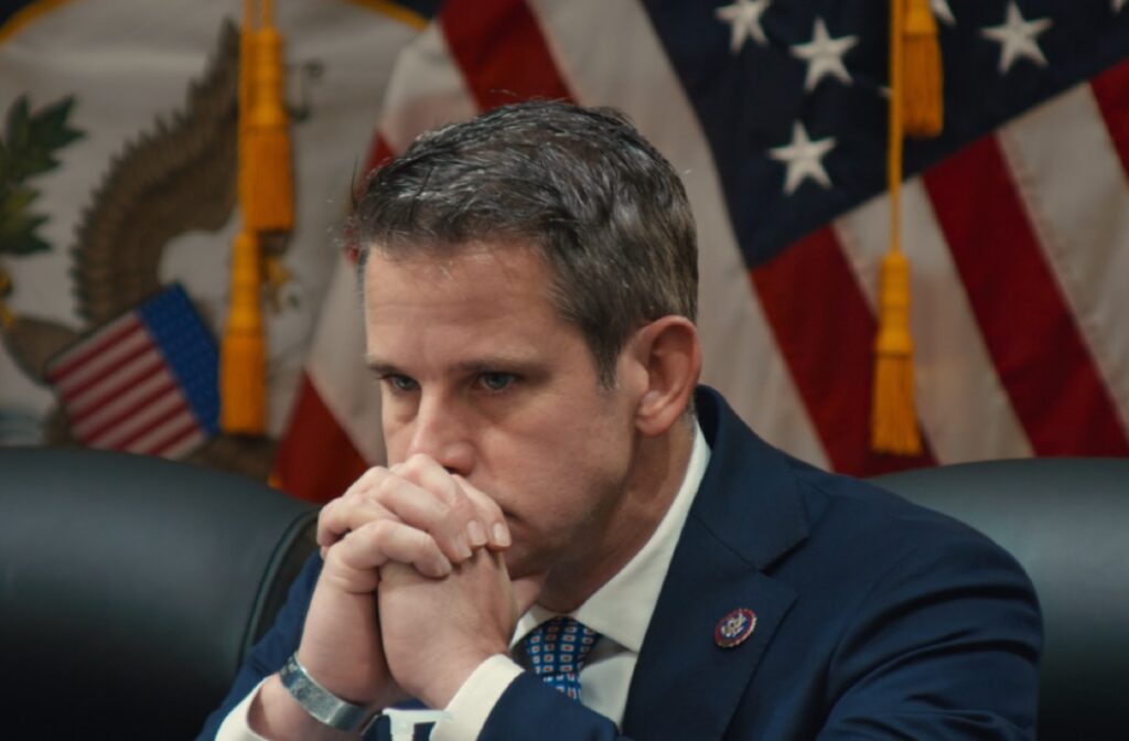 former congressman adam kinzinger in suit and tie with chin resting on his clasped hands during a congressional hearing