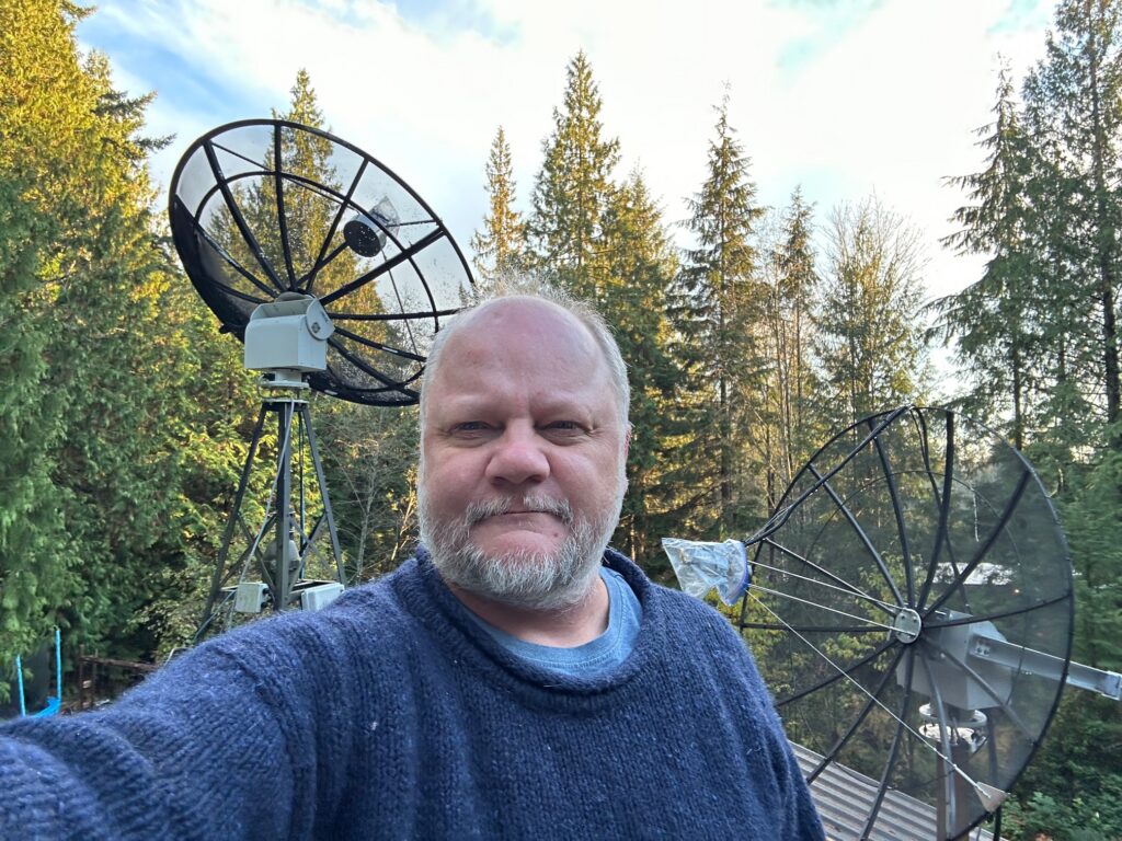 A man standing outdoors in front of two large antennas.