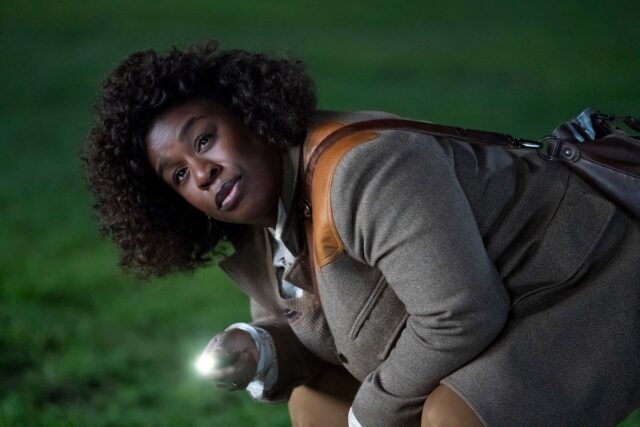 black woman crouched over on white house lawn with a flashlight at night