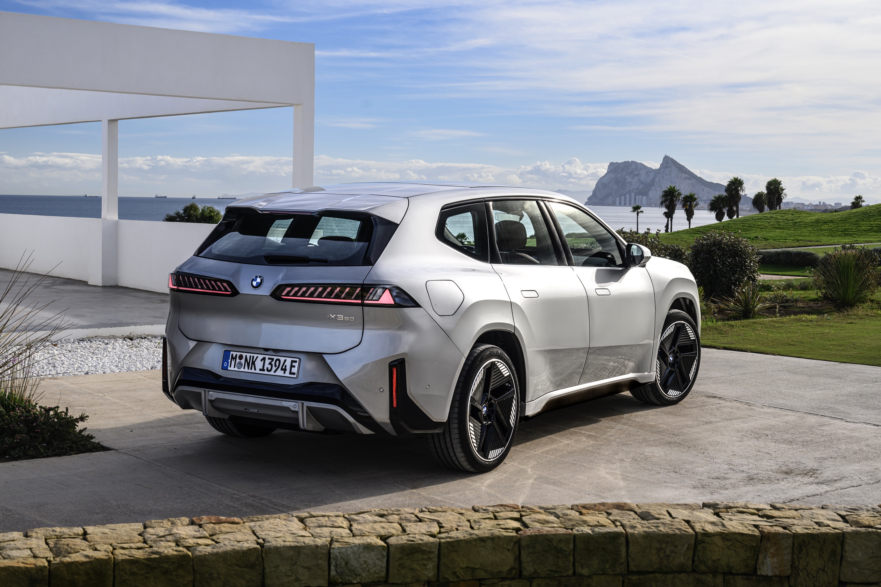 A BMW iX3 seen from the rear 3/4s, with Gibraltar in the distance