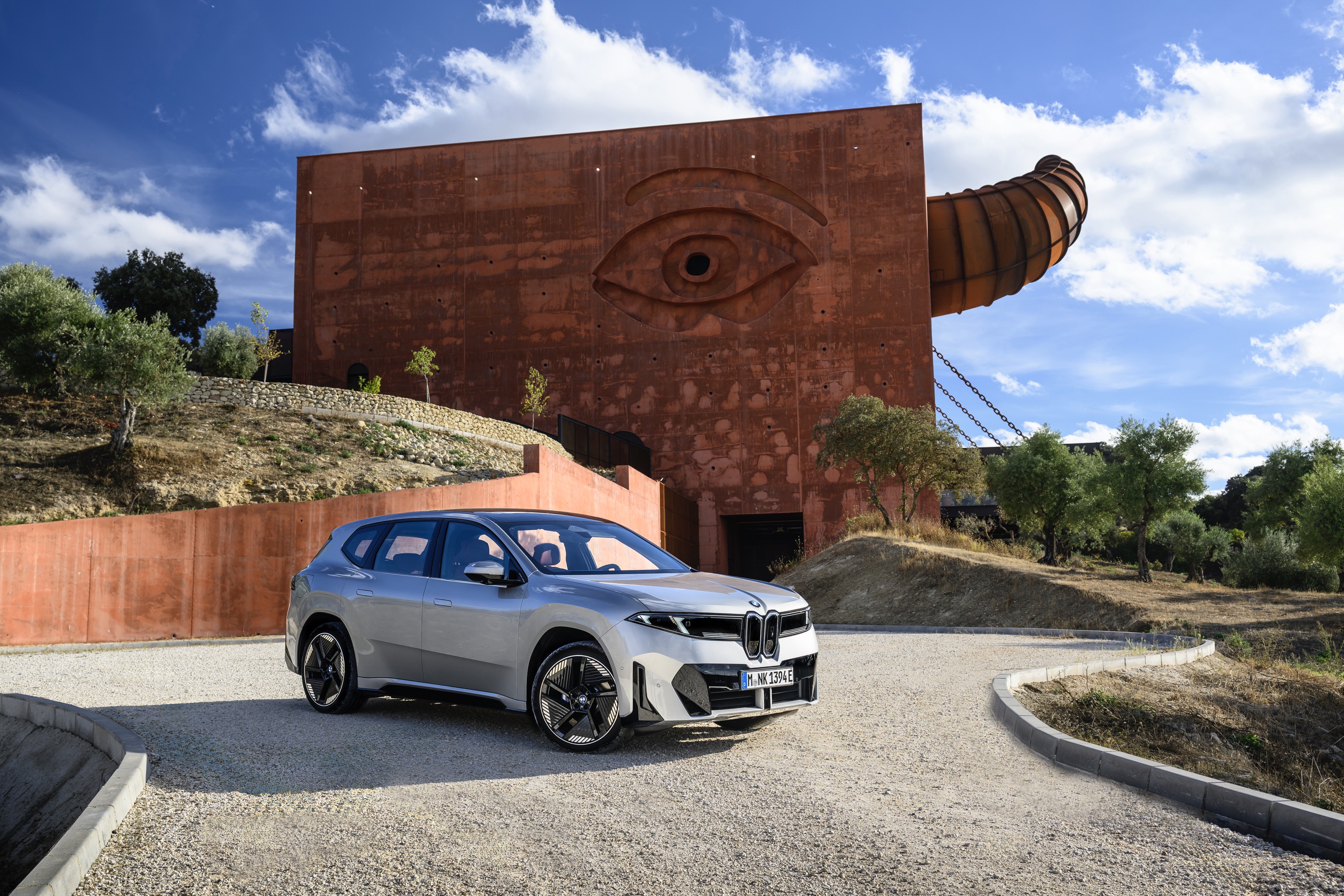 A silver BMW iX3 outside a building with a giant eye on its wall and a horn coming out the side.