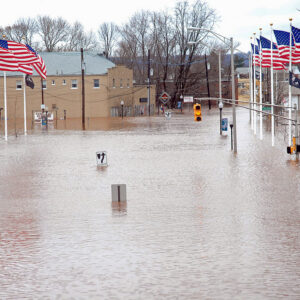 Photo of traffic lights above nearly submerged street signs, with flooded buildings in the backdrop.