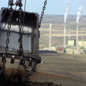 Image of a large metallic shovel suspended from chains in the foreground, with a coal generating plant in the background.