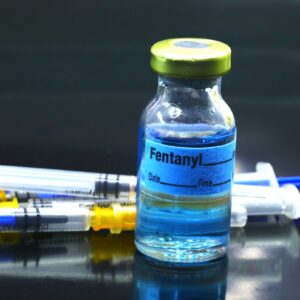 A vial of fentanyl with syringes behind it.