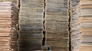 View of a single journal open in front of a huge stack of papers.