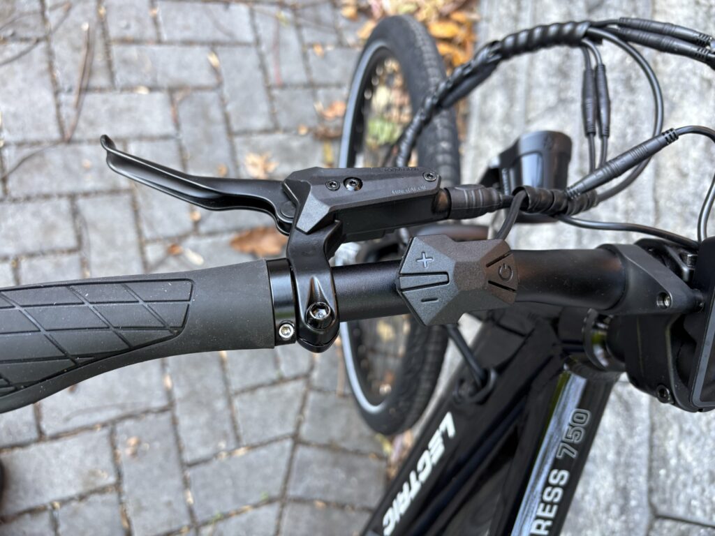 Image of the left handlebar of a bicycle, showing the brake lever and a three-button controller.