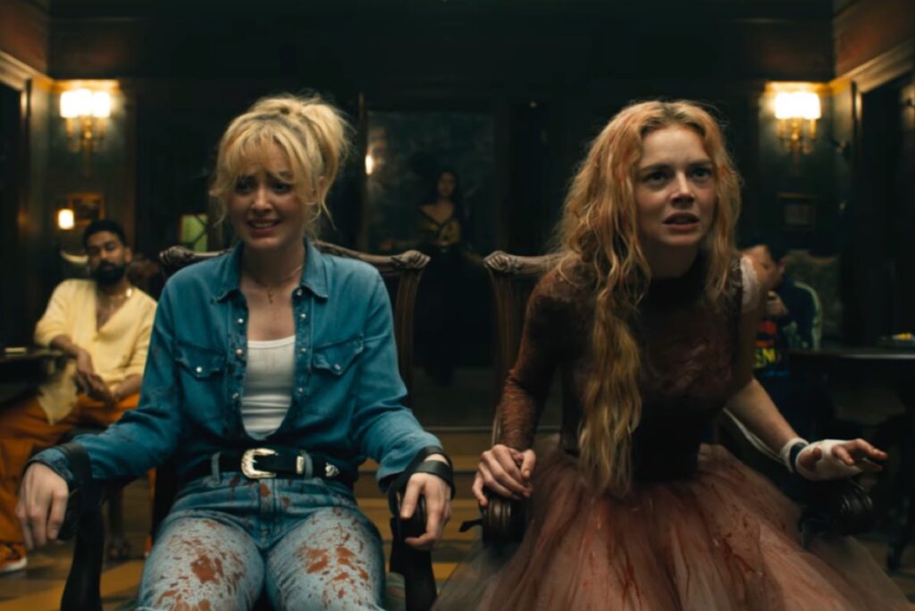 two blonde women tied to chairs, side by side.
