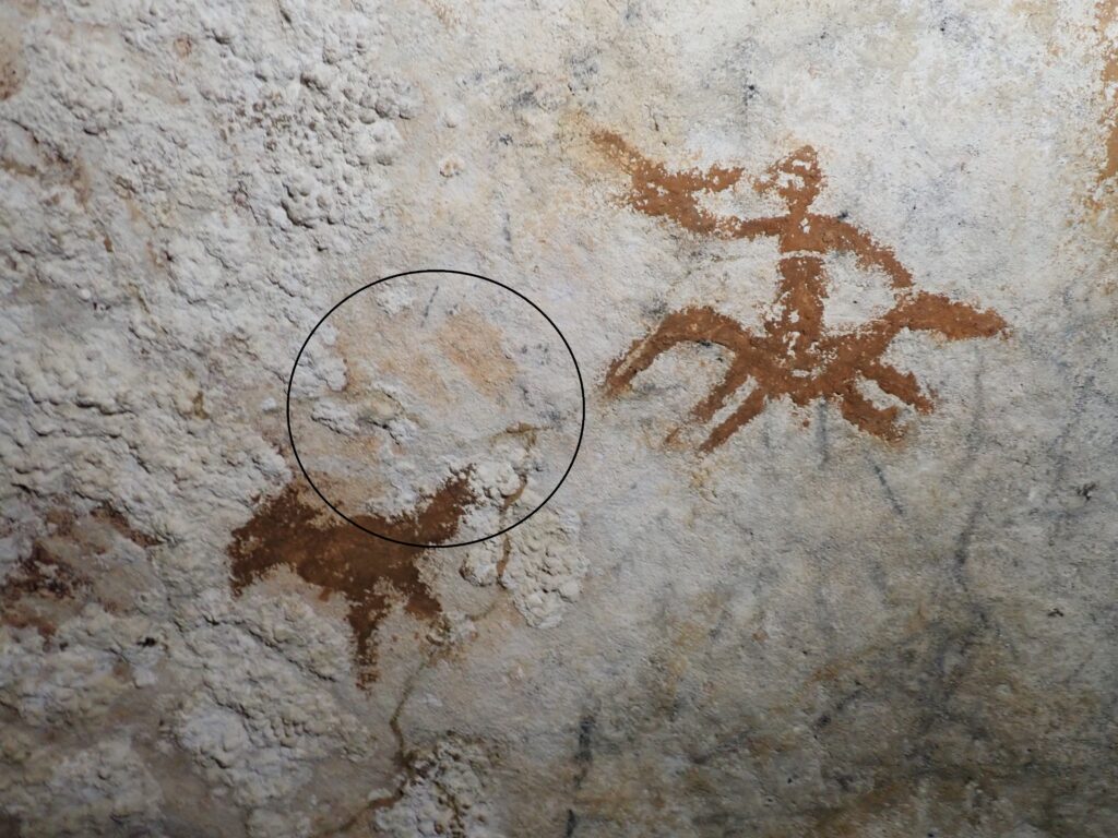 A photo of two figures on a cave wall, with the faint outline of a hand circled in black