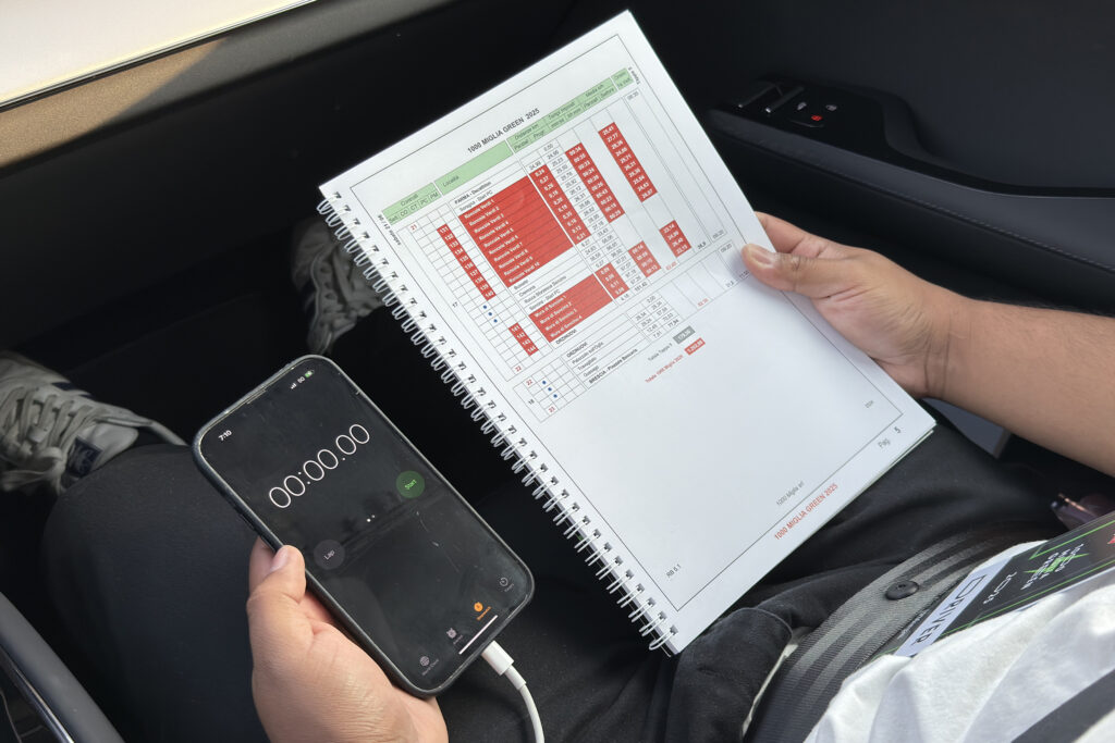 A man holds an iPhone running a timer and a book of numbers.