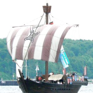 photo of a sailing ship with a single mast and a square sail painted red and white