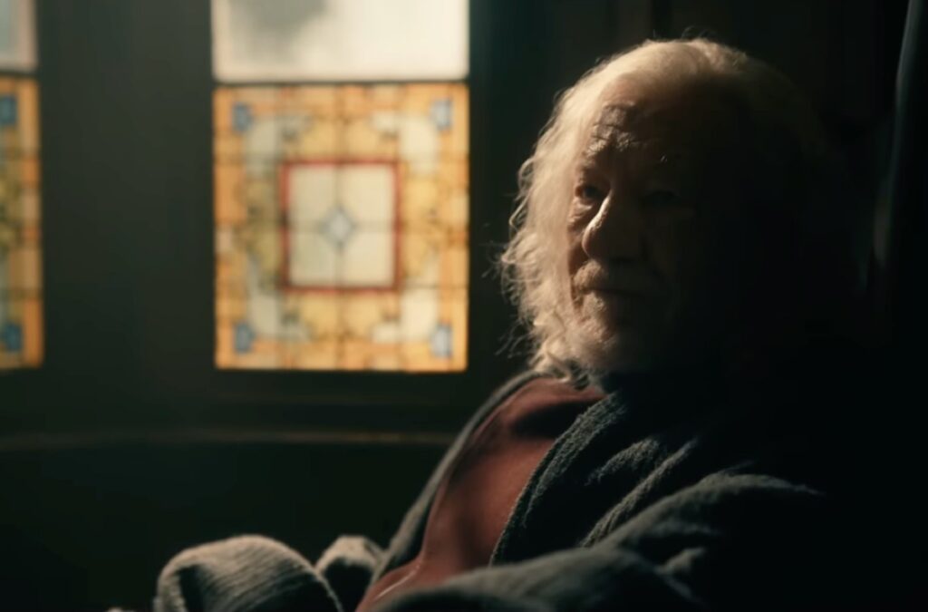 old man with white hair sitting in a chair by the window looking at someone seated in front of him