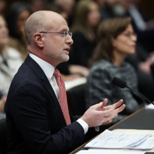 FCC Chairman Brendan Carr speaks into a microphone at a Congressional hearing. FCC Commissioner Anna Gomez sits next to Carr.