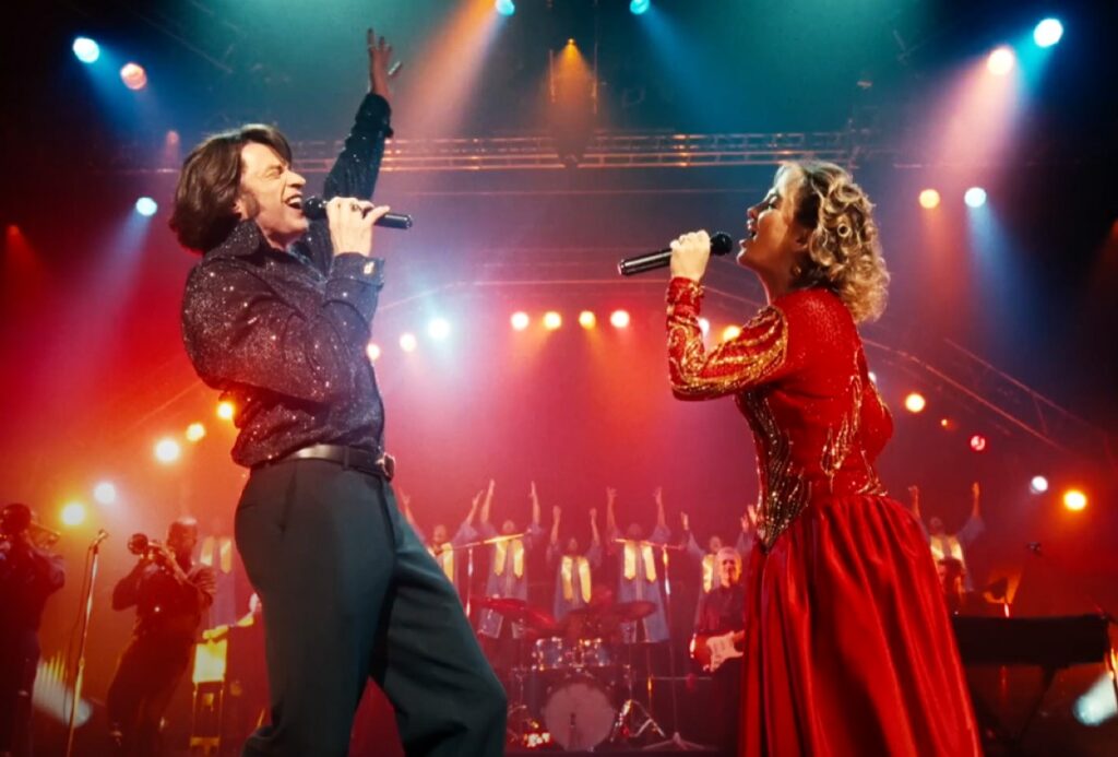 msn and woman onstage singing. Man is dressed as Neil Diamong, woman is in a long red dress.