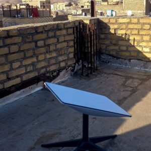A Starlink satellite dish sitting on top of the upper part of a house in an area enclosed by short brick walls.