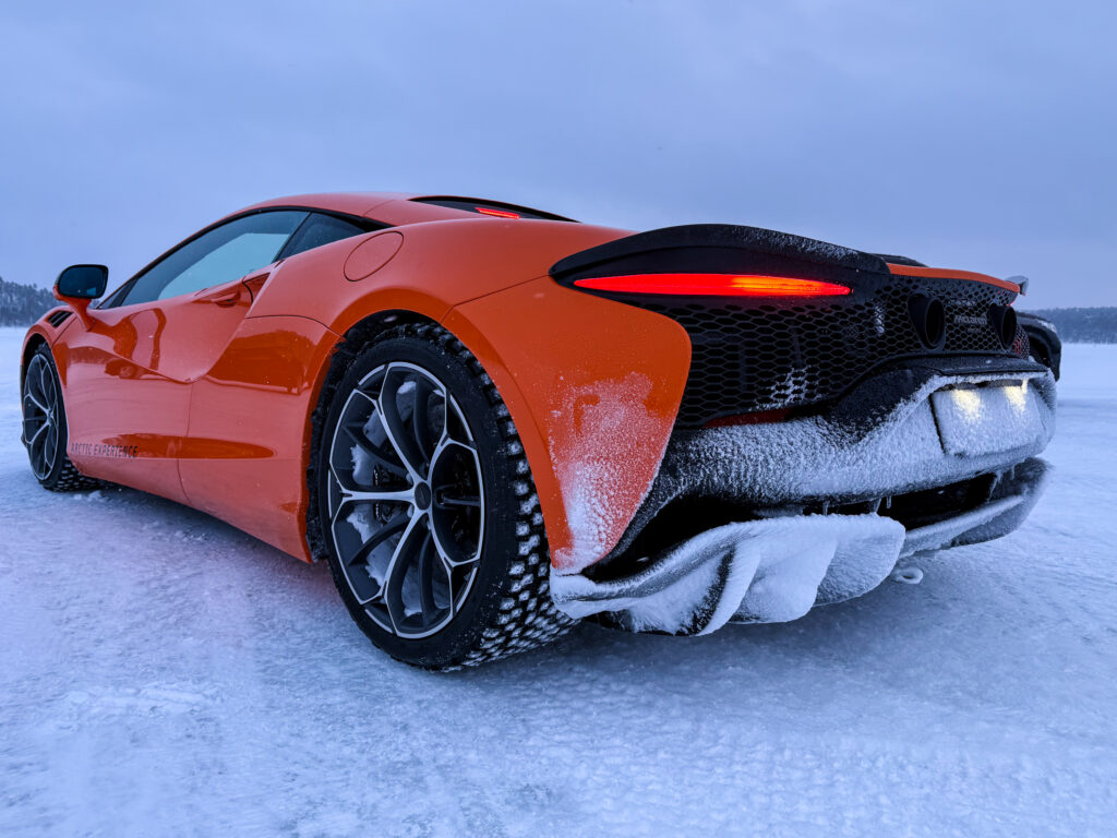 An orange McLaren Artura, seen from behind on a frozen lake. The rear is encrusted with snow.