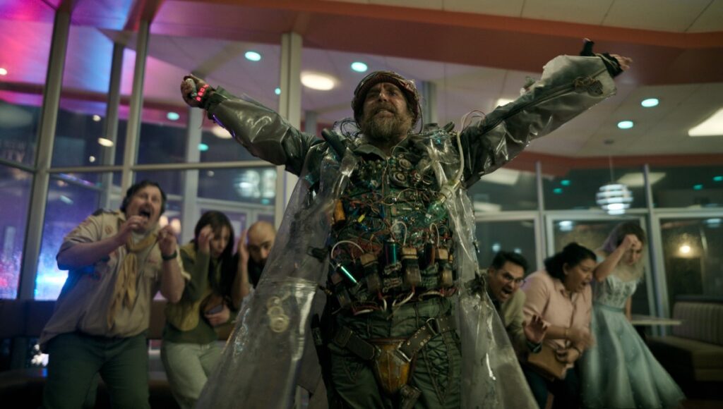 crazed looking man opening his jacket to reveal a bomb strapped to his chest while standing in a diner