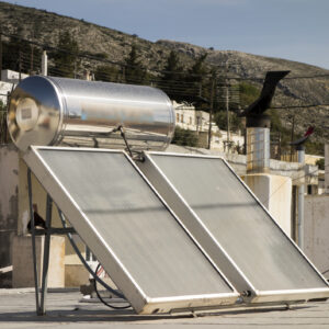 Image of two panels in the sunlight, topped by a silver tank to store water heated by the system.