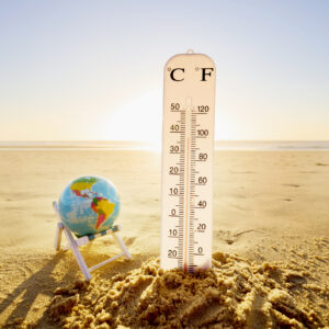 a sandy beach with a globe balanced in a beach chair next to an oversized thermometer showing high temperatures.