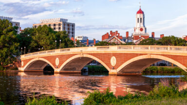 A red brick arched bridge, with a white tower behind it.
