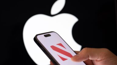 The Apple News logo is displayed on a mobile phone screen in front of a computer screen displaying an Apple logo