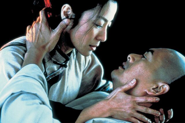 Asian woman holding a dying Asian, his hands reaching up to cup her face.
