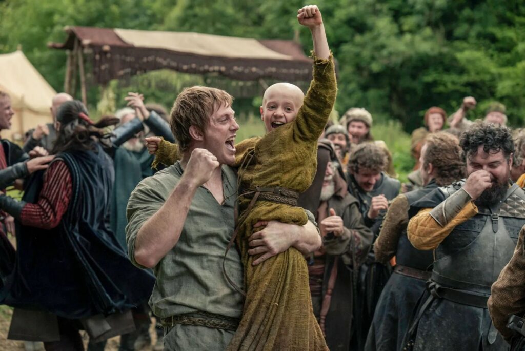 man holding a young bald boy up as both cheer wildly.