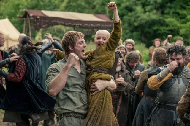 Một người đàn ông đang bế một cậu bé hói đầu lên, cả hai cùng reo hò cuồng nhiệt.