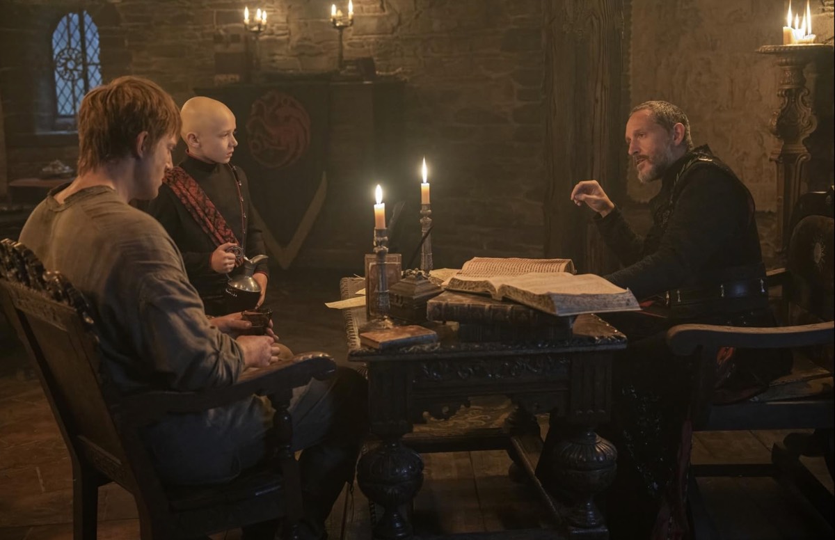 Một chàng trai trẻ và một đứa trẻ hói đầu ngồi trước mặt một vị hoàng tử lớn tuổi hơn tại bàn làm việc của ông ta.