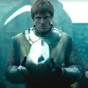 Knight in full armor staring into the camera while holding his helmet