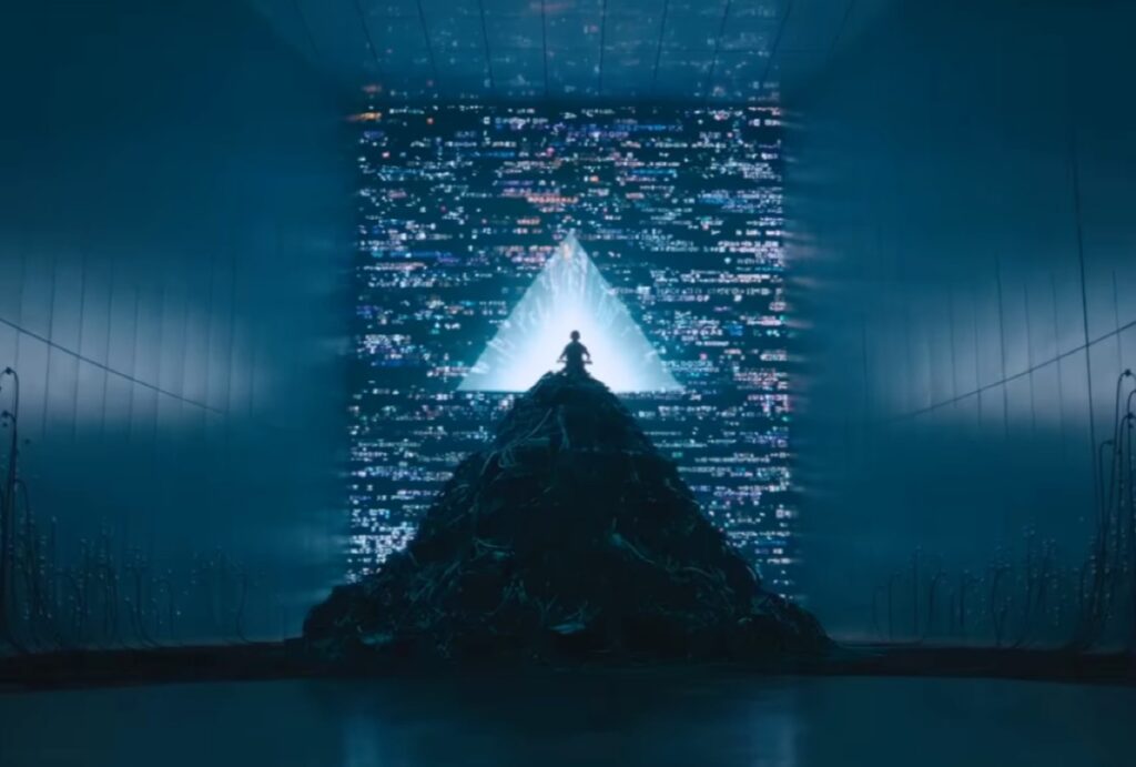 blue-hued image of a small boy sitting on a pile of electronic refuse, tapping on a laptop computer in front of a giant screen with a glowing blue triangle in the middle