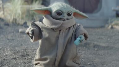 little green yoda-like alien holding a light blue sweet treat shaped like a small cookie.