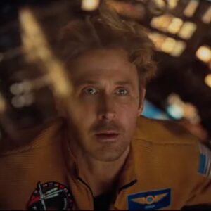 closeup of blond man in a spacesuit peering out through a window of his spacecraft in wonder