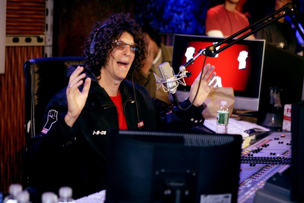 Howard Stern talking in a studio and gesturing with his hands during his radio show.