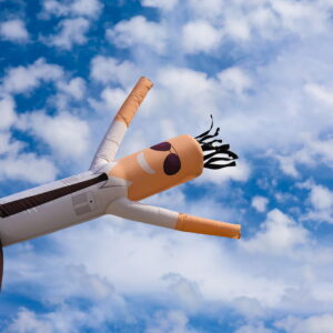An inflatable tube man, or sky puppet dancer, frolics in the sky over an event in Camarillo, California. The inflatable male figure wears dark sunglasses, a white long-sleeved dress shirt, dark tie and dark dress pants.